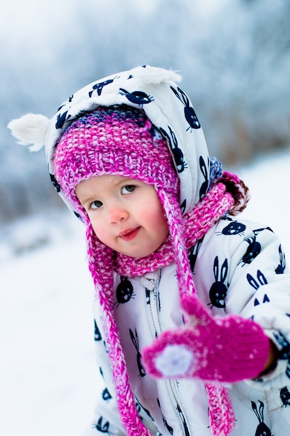 Petite fille en blanche chapeau de neige et rose, bottes et gants dans le parc d'hiver de neige.