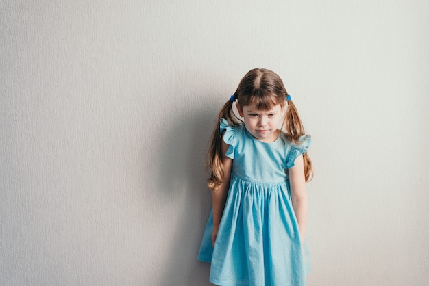 Petite fille blanche en colère en robe bleue sur fond neutre