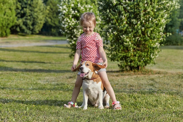 Petite fille blanche joue avec une séance photo de chien beagle en été dans la rue