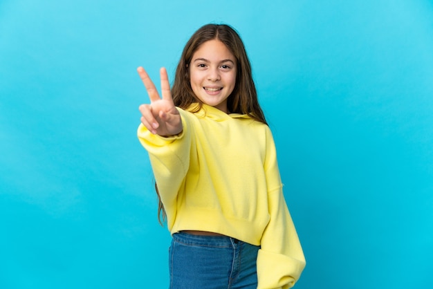 Petite fille sur bleu isolé souriant et montrant le signe de la victoire