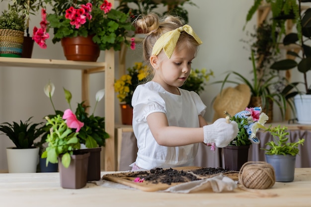 petite fille blonde avec un arc sur la tête plantes et greffes et arrose les fleurs d'intérieur