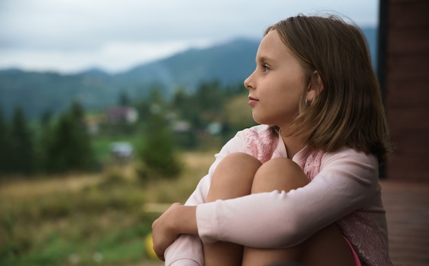 Petite fille blonde assise en plein air et regardant la vue sur la montagne