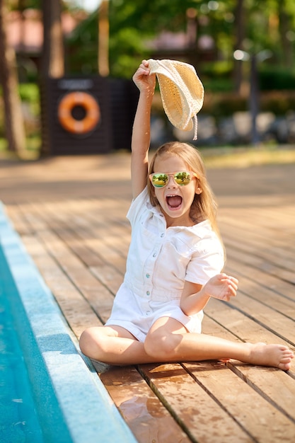 Une petite fille blonde assise près de la piscine