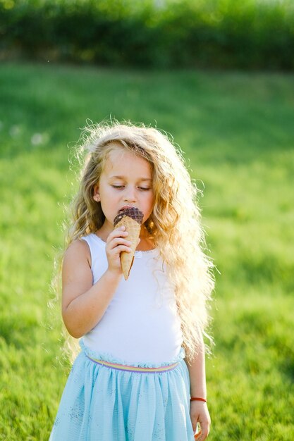 Petite fille blonde aux cheveux longs s'amuse à manger des glaces dans un parc d'été.