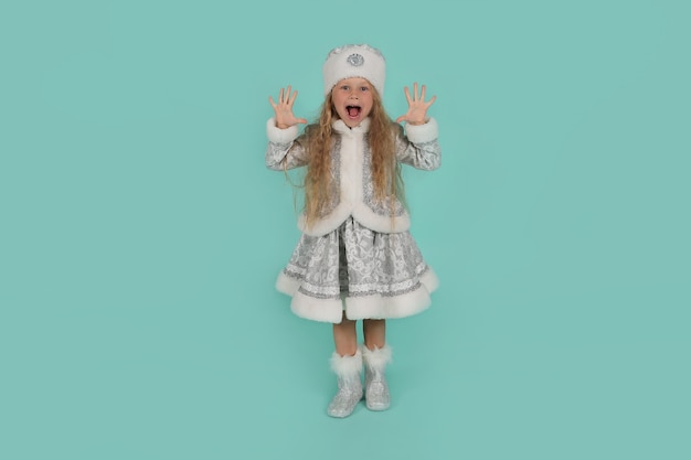 Une petite fille blonde aux yeux bleus dans un costume de jeune fille des neiges du Nouvel An sur fond bleu