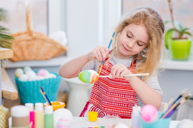 Petite fille blonde à colorier des œufs pour les vacances de Pâques à la maison.