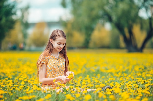 Petite fille blonde cueillir des fleurs dans un pré plein de pissenlits jaunes