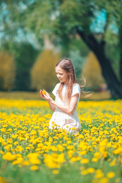 Petite fille blonde cueillir des fleurs dans un pré plein de pissenlits jaunes