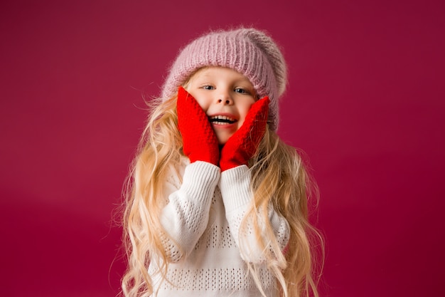 petite fille blonde dans un bonnet tricoté et des mitaines sourit. vêtements d'hiver