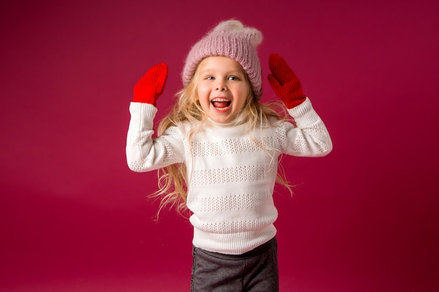 petite fille blonde dans un bonnet tricoté et des mitaines sourit. vêtements d'hiver