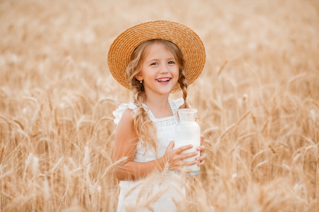 Petite fille blonde dans un champ de blé mange du pain et boit du lait