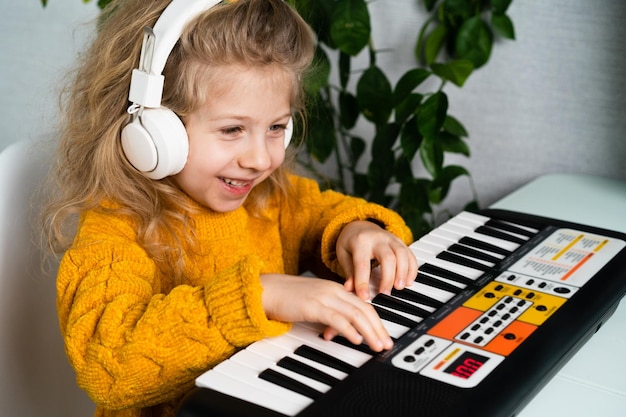 Une petite fille blonde dans des écouteurs souriant et jouant du synthétiseur le concept d'enseignement