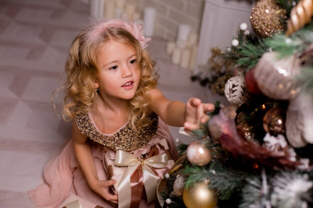 petite fille blonde décore le sapin de Noël dans un bel intérieur