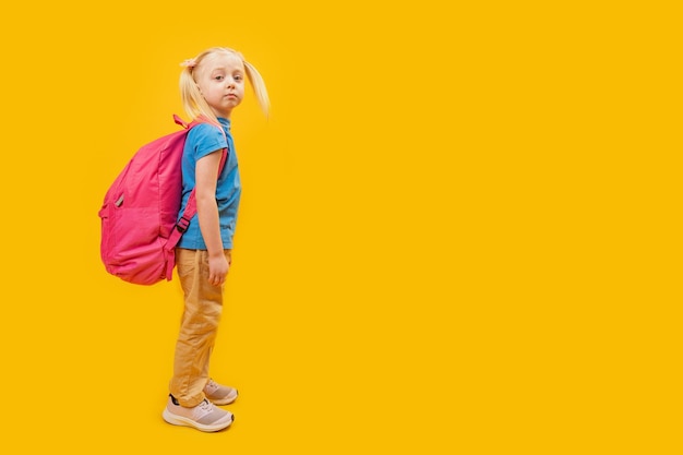 Petite fille blonde avec deux queues de cheval avec un grand sac à dos d'école Portrait en pied de l'enfant vue latérale Espace de copie Première fois à l'école