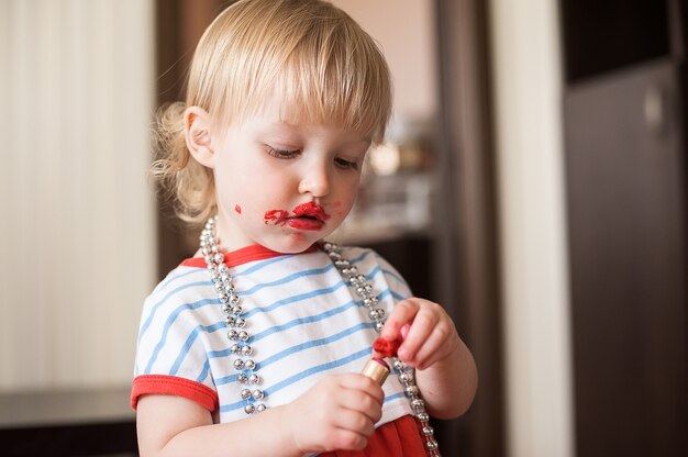 Petite fille blonde drôle maquillage lèvres avec rouge à lèvres de maman. Apprendre à être une femme.