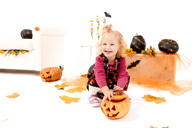 Petite fille blonde drôle et mignonne de courbe avec la citrouille dans la décoration d'Halloween