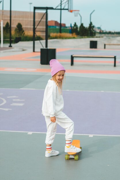 Une petite fille blonde fait du skateboard sans protection.