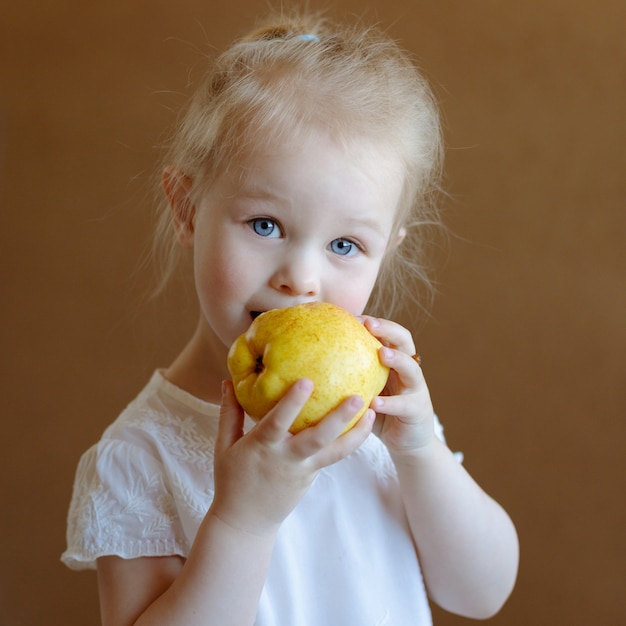 La petite fille blonde mange une poire jaune