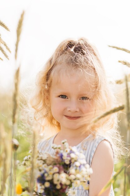 Petite fille blonde mignonne avec un bouquet des fleurs sauvages en nature pendant l'été