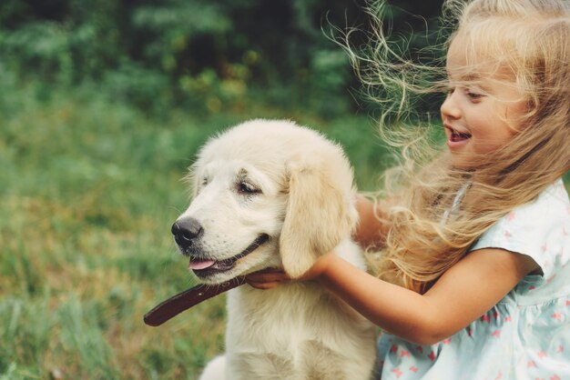 Petite fille blonde mignonne jouant avec son chiot golden retriever en été dans le parc.