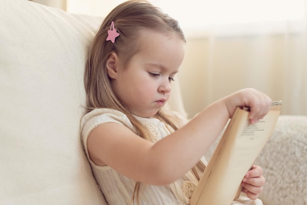 Petite fille blonde mignonne lisant un livre assis sur un canapé Enfant lisant le rêve et le développement de l'imagination Journée internationale du livre pour enfants Les enfants adorent lire la Journée mondiale du livre