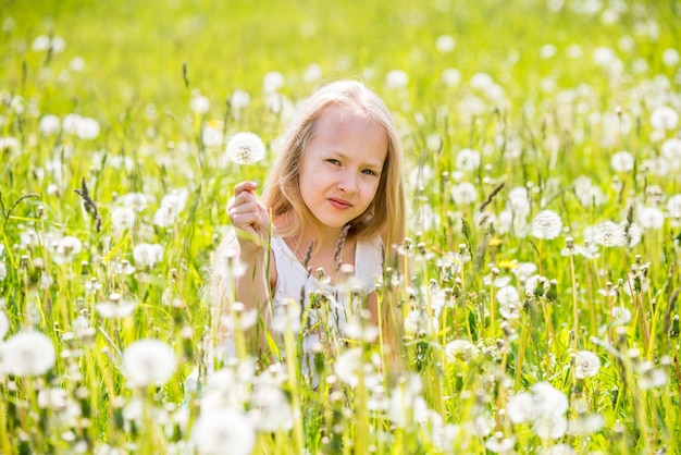 Petite fille blonde mignonne avec pissenlit dans un pré blanc