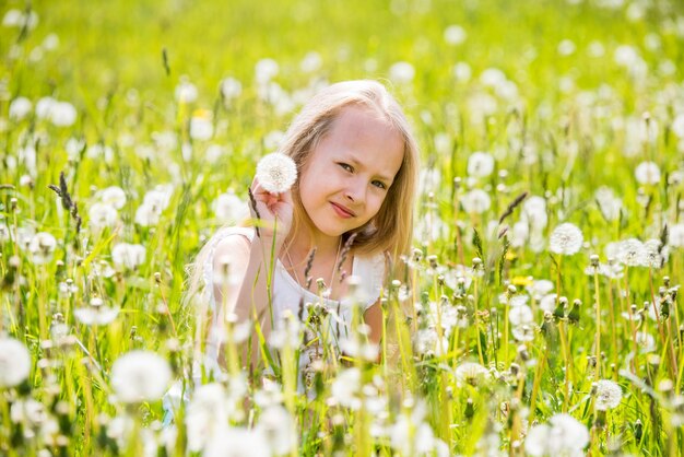 Petite fille blonde mignonne avec pissenlit dans un pré blanc