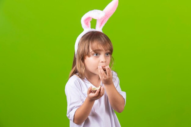 Petite fille blonde avec des oreilles de lapin en chocolat sales mangeant des oeufs de Pâques