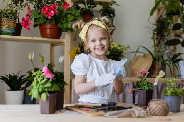 petite fille blonde portant des gants de travail plantes et greffes et eaux fleurs d'intérieur
