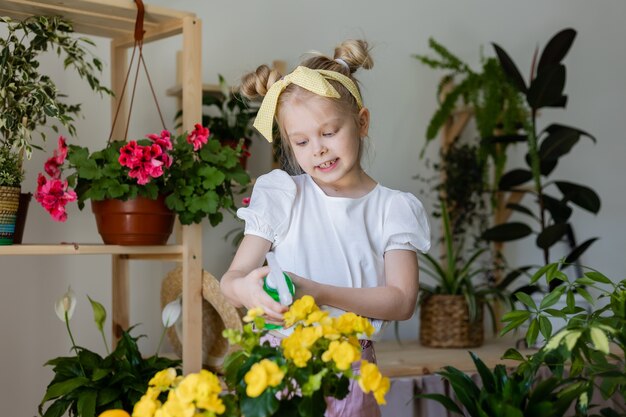 petite fille blonde pulvérise d'un distributeur de balles ou arrose des fleurs d'intérieur Jardinage à la maison