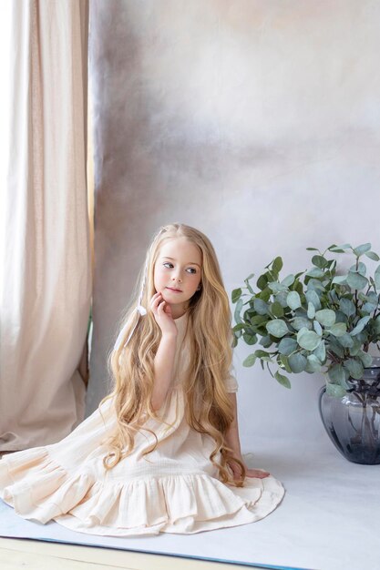 Photo petite fille blonde en robe vintage près de fond rétro et vase avec des branches vertes eucalyptus gum tree enfance heureuse vie simple et confortable heureuse chasse aux œufs de pâques