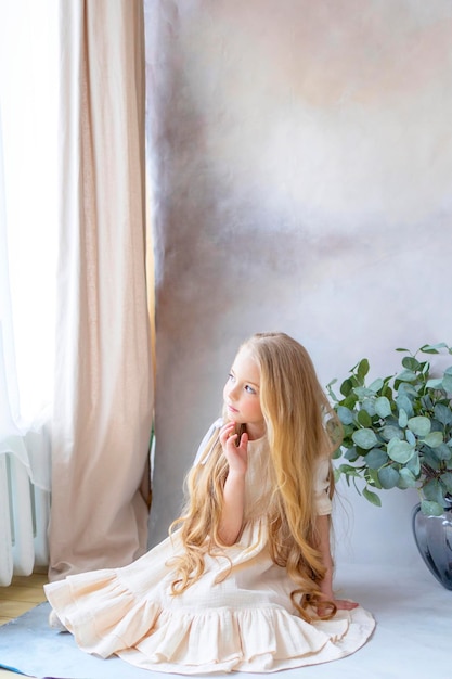 Photo petite fille blonde en robe vintage près de fond rétro et vase avec des branches vertes eucalyptus gum tree enfance heureuse vie simple et confortable heureuse chasse aux œufs de pâques