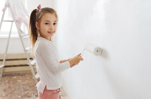 petite fille blonde avec un rouleau de peinture murale pendant la rénovation domiciliaire