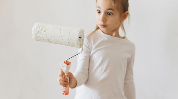 petite fille blonde avec un rouleau de peinture murale pendant la rénovation domiciliaire