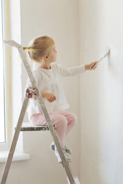 petite fille blonde avec un rouleau de peinture murale pendant la rénovation domiciliaire