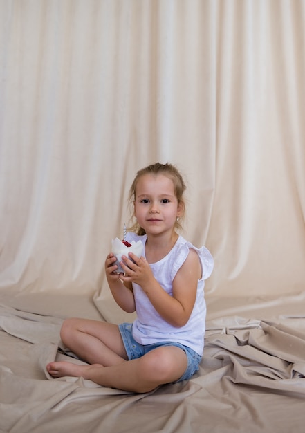 Petite fille blonde s'assoit et tient un cupcake festif avec une bougie sur fond beige avec une copie de l'espace