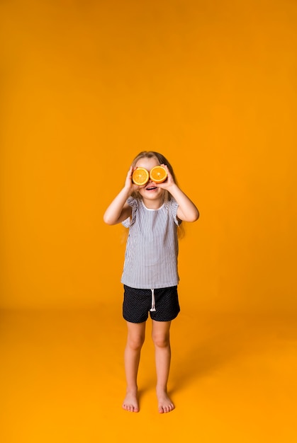 Une petite fille blonde se lève et ferme les yeux avec une demi-orange sur une surface jaune avec un espace pour le texte