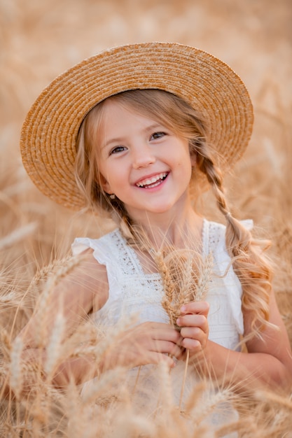 Petite fille blonde se promène dans un champ de blé d'été