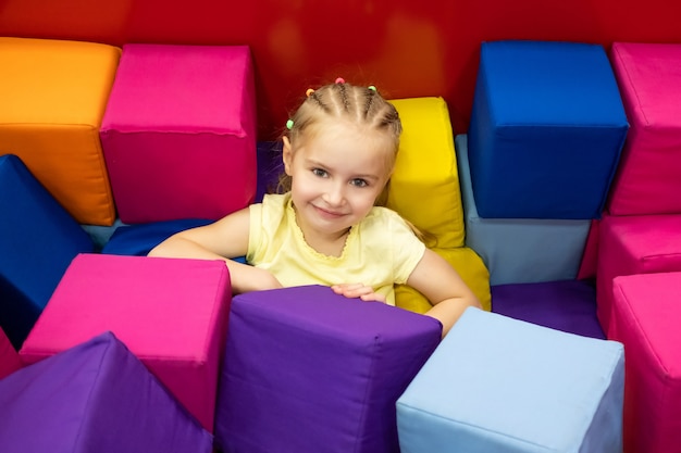 Petite fille blonde souriante assise dans la salle de jeux