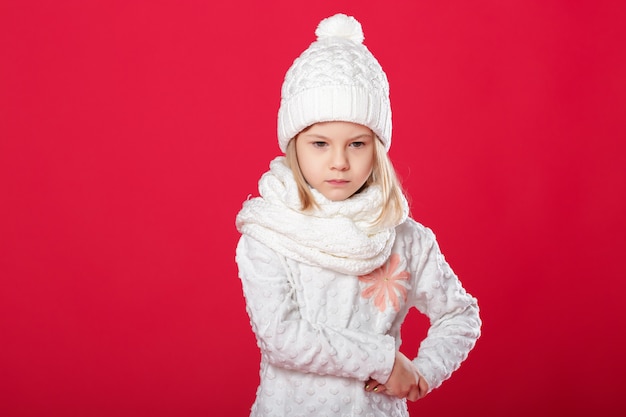Petite fille blonde souriante dans un chapeau blanc et une écharpe rouge