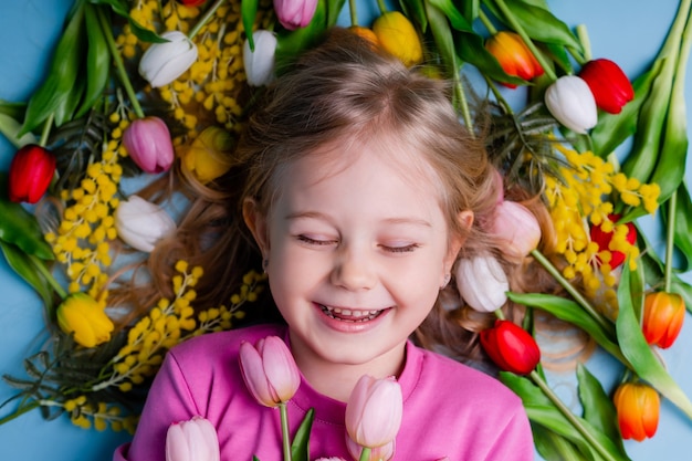 Petite fille blonde tenant un bouquet de tulipes sur fond bleu en studio