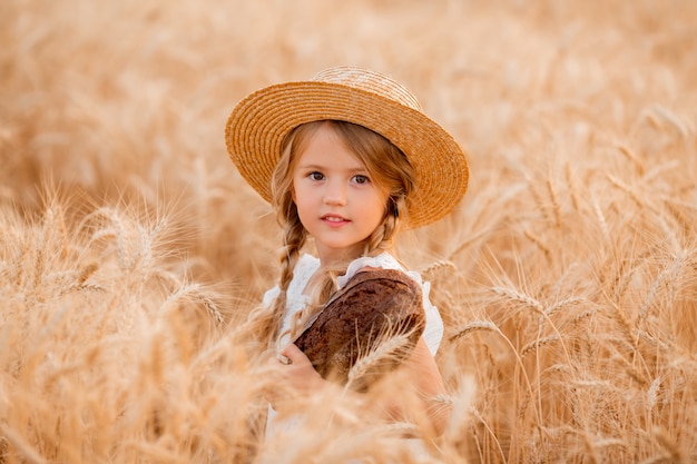 Petite fille blonde tient une miche de pain frais dans un champ de blé en été