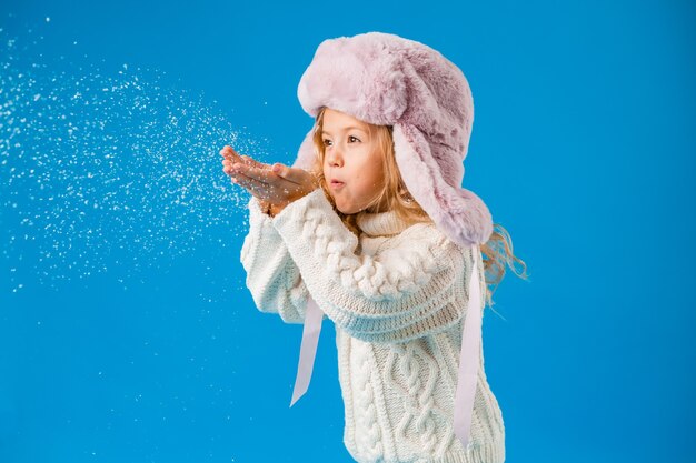 Petite fille blonde en vêtements d'hiver souffle la neige sur ses mains