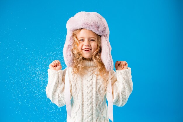 Petite fille blonde en vêtements d'hiver souffle la neige sur ses mains