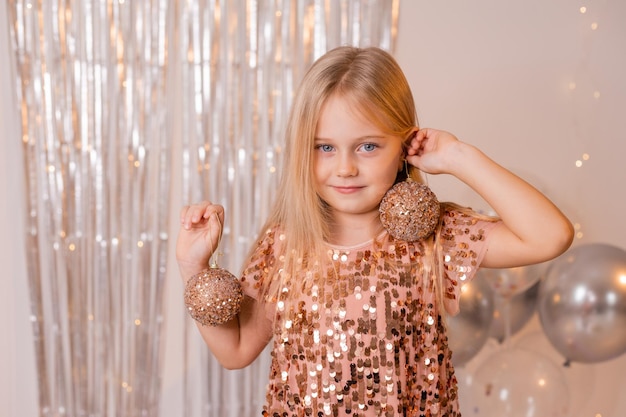 une petite fille blonde vêtue d'une robe brillante joue avec des boules de Noël au carnaval du Nouvel An