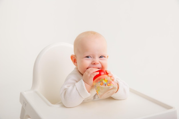 Une petite fille boit de l'eau d'une bouteille à l'intérieur est assise sur une chaise haute