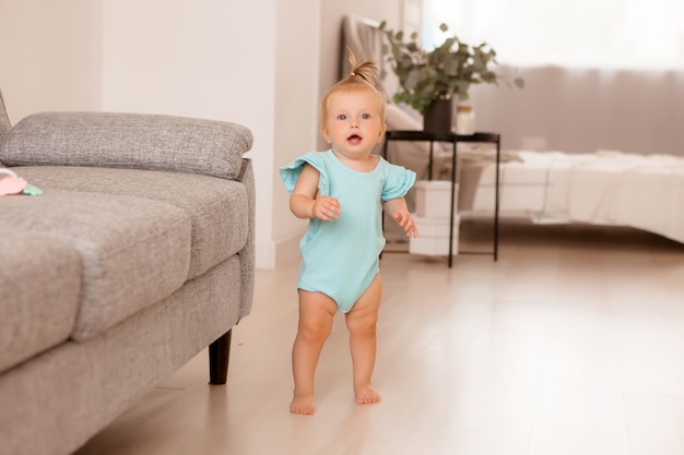 Petite fille en bonne santé dans une pièce à côté d'un canapé gris apprend à marcher