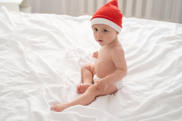 Petite fille en bonnet de noel jouant s'amusant sur une literie blanche sur le lit