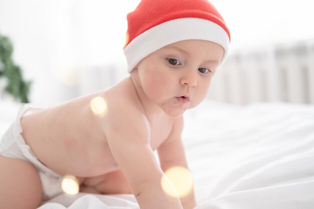 Petite fille en bonnet de noel jouant s'amusant sur une literie blanche sur le lit