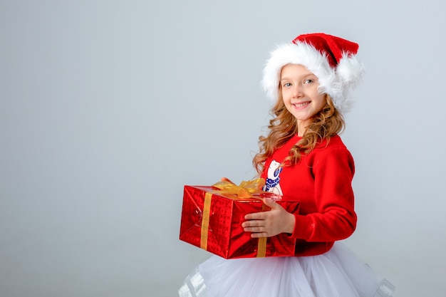 Petite fille en bonnet de Noel tenant un cadeau sur fond blanc